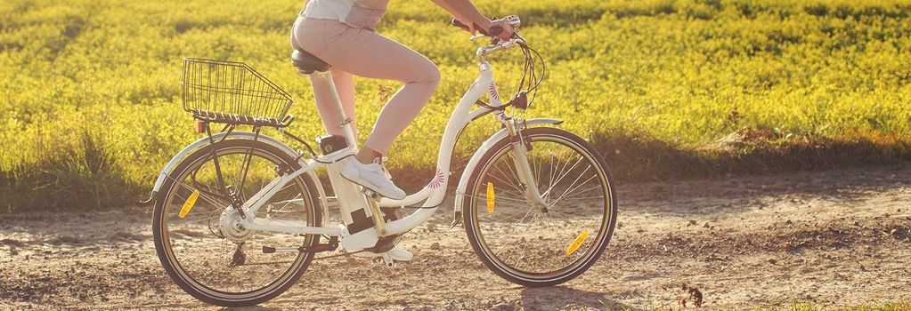 Eine Frau fährt ein E-Bike mit tiefem Einstieg für Senioren auf einem Feldweg. Hinter ihr eine grüne Wiese im Sonnenuntergang.