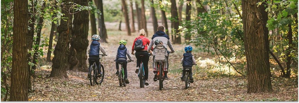 Eine Fahrradtour mit Kindern: Vater, Mutter und 3 Kinder fahren, ein weiteres Kind befindet sich auf dem Kindersitz. Szene: Wald