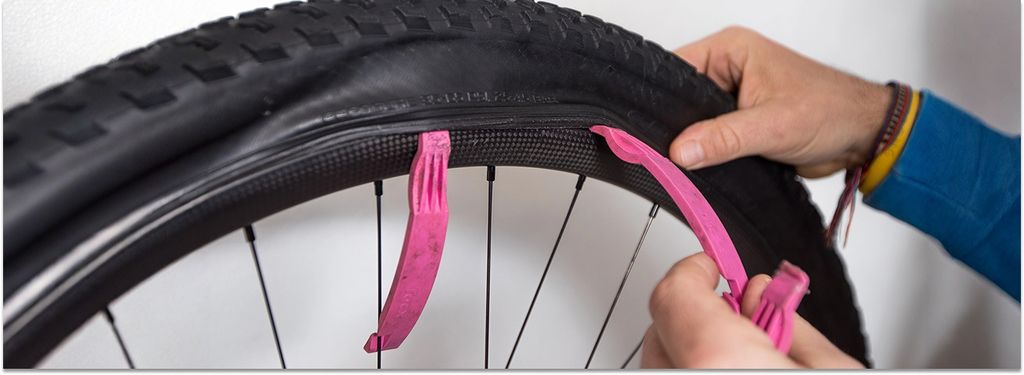 Reparatur von Fahrradschläuchen. Eine Hand einer Person entfernt mit Hilfe pinkfarbener Reifenhebel einen Reifen an einem Carbon-Mountainbike-Rad.