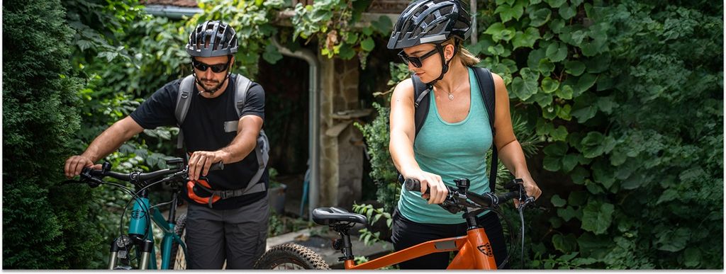 Ein Mann und eine Frau schieben ihre E-Bikes. Sie tragen jeweils einen schwarzen Helm auf dem Kopf