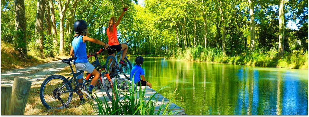 Eine Familie mit Kindern mach mit ihren Fahrrädern eine Pause an einem Kanal. Links und rechts sind Bäume zu sehen.
