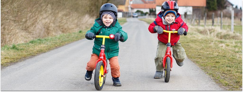 Zwei Kinder fahren schnell mit ihrem Laufrad auf den Fotografen zu und lachen dabei.