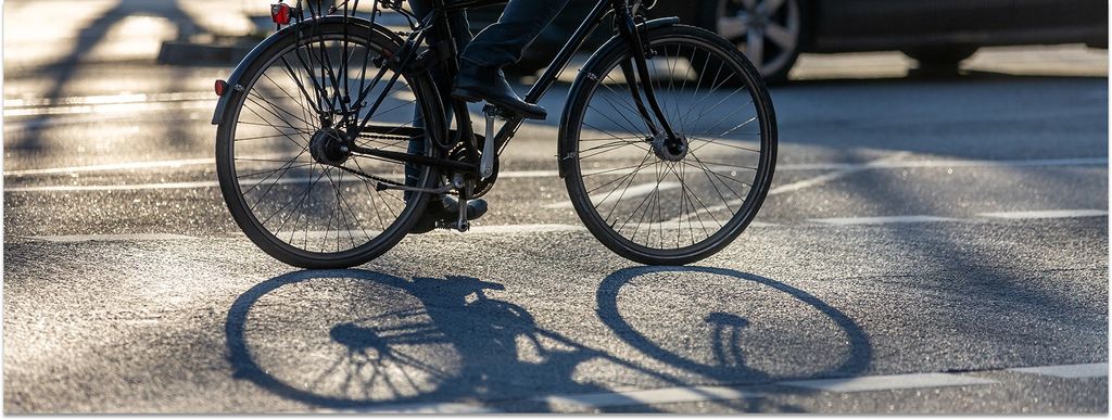 Ein Radfahrer fährt auf der Straße, hinter ihm die Sonne, er wirft einen Schattenn.