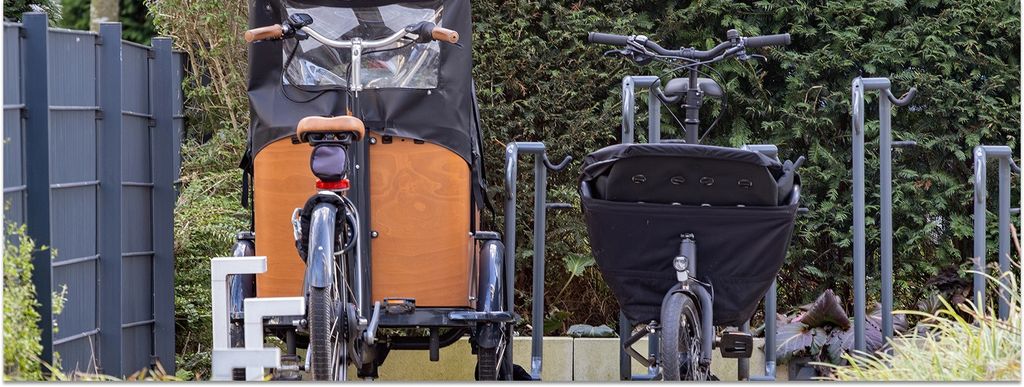 Zwei verschiedener Lastenräder stehen geparkt in einem Hof.
