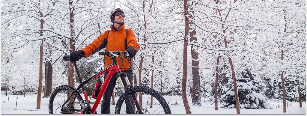 Ein Mann mit orangefarbener Jacke und rotem Fahrrad steht im Winter im schneebedeckten Wald